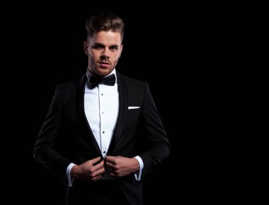 Genç damat siyah arka plan üzerine ceketini'nın düğmesini tutarak önden görünümü