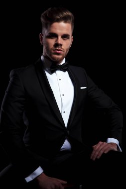 oturma ve siyah arka plan üzerine kameraya bakarak zarif delikanlı önden görünümü