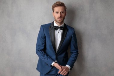 Zarif adam açık gri renkli yüzünde hafif bir gülümseme yazabilmek elele mavi bir smokin giyiyor