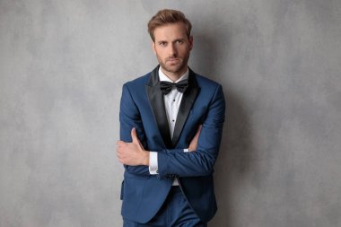 İyi giyimli adam mavi ceketli ellerini tutarak bir ışık gri arka plan üzerinde çarpı işareti