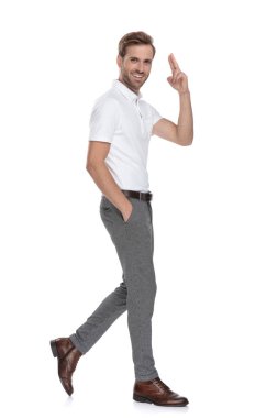 Casual adam cebinde el ile gülümseyerek yürüyen ve beyaz arka plan üzerinde selamlayan