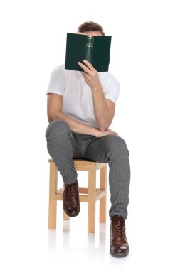 casual adam oturuyor ve beyaz arka plan ile o yüzü kapsayan bir kitap okuma