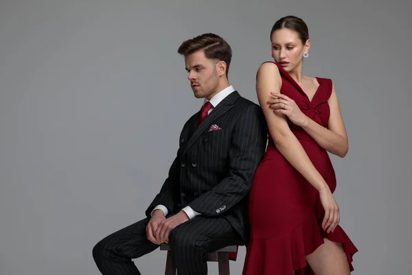 背靠背优雅的夫妇摆姿势在工作室 男人坐在凳子上 女人触摸她的手臂在灰色的背景 — 图库照片