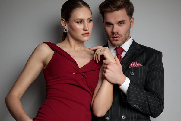 elegant man holding his woman's wrist in a pose on grey background