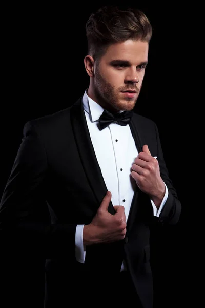 Young Elegant Man Puliing His Tuxedo Collars While Looking Away — Stock Photo, Image