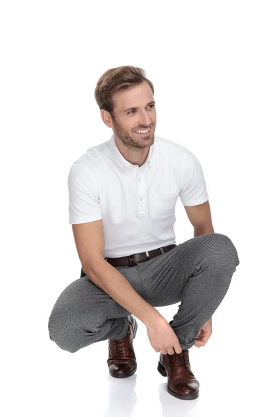 微笑的休闲男子绑他的鞋 而蹲在白色的背景 — 图库照片