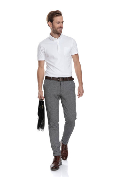 счастливый молодой умный случайный человек ходит с чемоданом и смотрит в сторону на белом фоне
