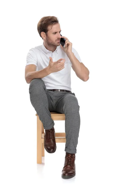 Homem Confuso Sentado Gesticulando Confusão Falar Seu Telefone Fundo Branco — Fotografia de Stock