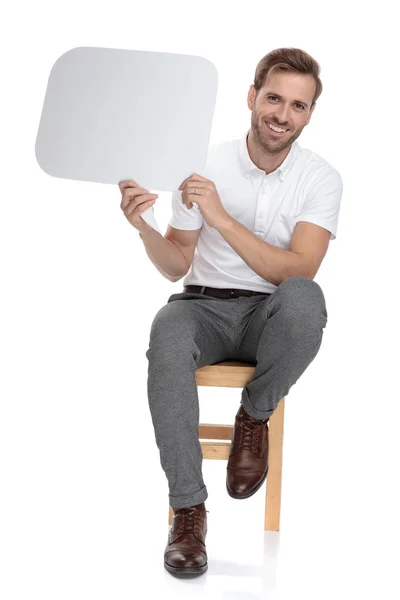 坐在椅子上的随意男子拿着一个空白的讲话泡沫在白色背景 — 图库照片