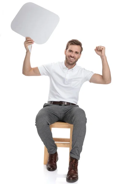 Sentado Casual Homem Celebra Enquanto Segurando Discurso Bolha Fundo Branco — Fotografia de Stock