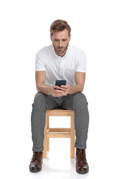 Homem Casual Lendo Seu Telefone Enquanto Sentado Uma Cadeira Fundo — Fotografia de Stock