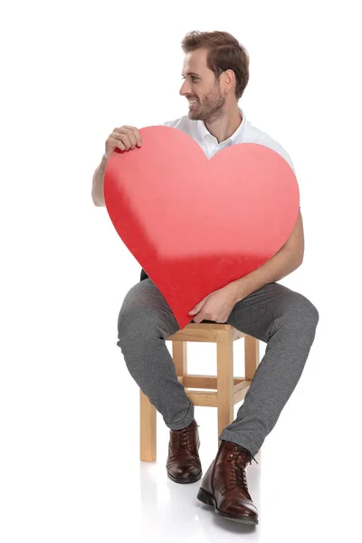 Sentado Homem Segurando Grande Coração Vermelho Olha Para Lado Fundo — Fotografia de Stock