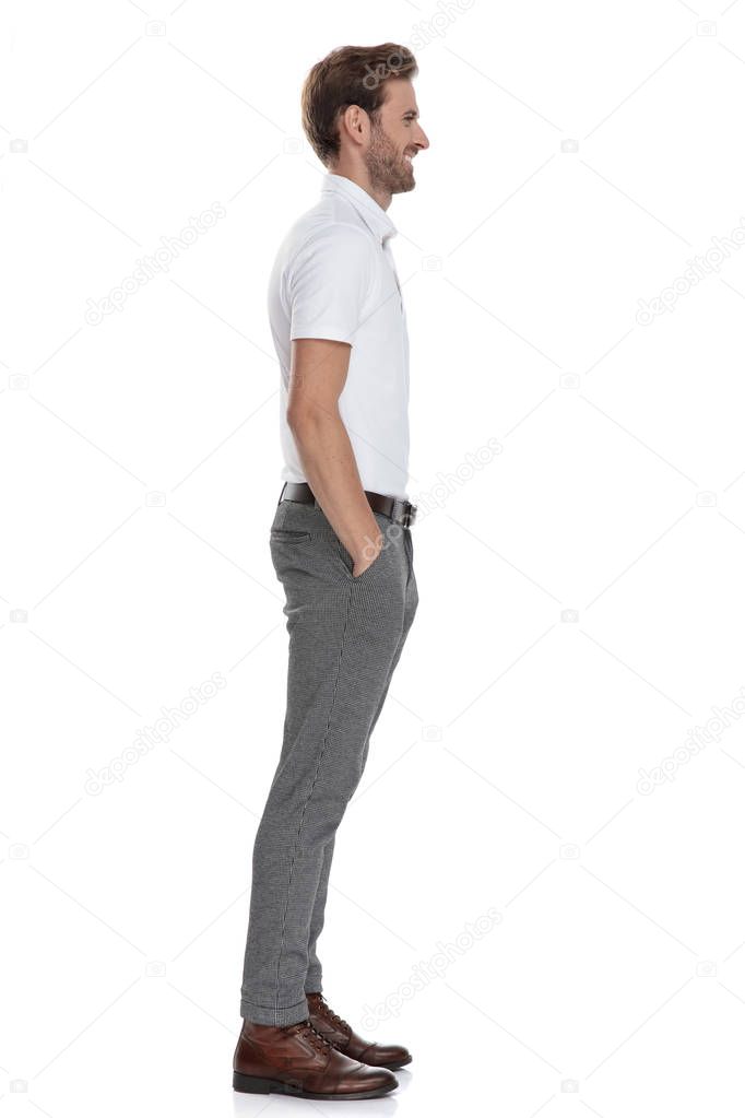 side view of a smiling casual man with hands in pockets, waiting in line on white background