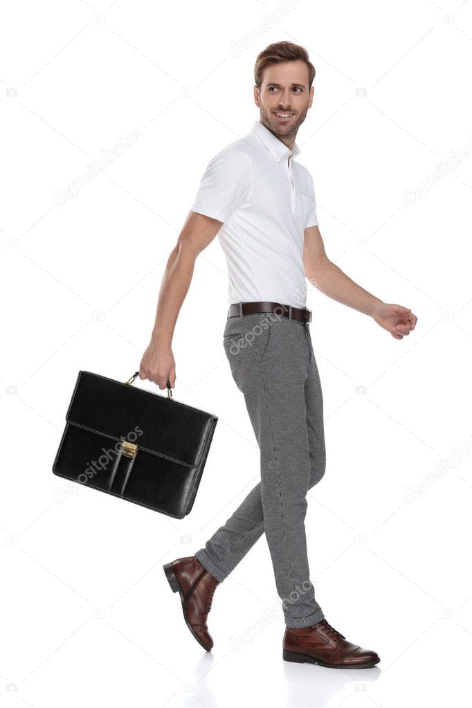 side view of a walking smart casual man holding briefcase and looking back on white background