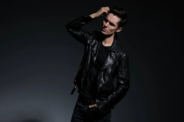 Dramatic young man in leather jacket fixes his hairstyle — Stock Photo, Image