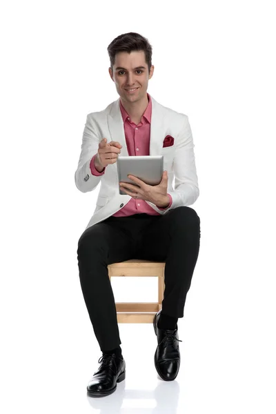 Sonriente hombre elegante sentado con la tableta y el dedo que apunta — Foto de Stock