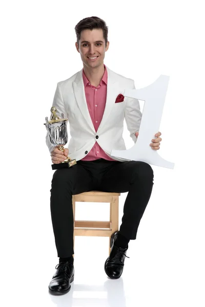 Улыбающийся элегантный чемпион сидит и держит свои призы — стоковое фото