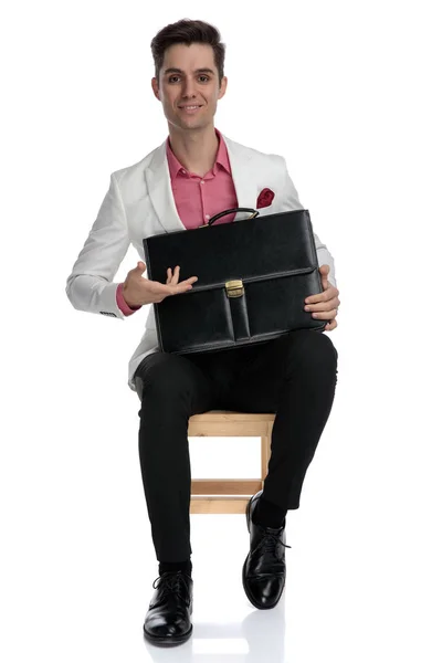 Giovane uomo d'affari sorridente seduto e presentando la sua valigetta — Foto Stock