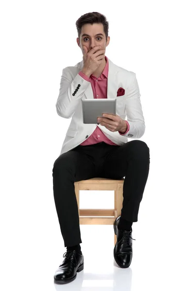Jovem homem de negócios sentado lendo notícias surpreendentes em seu tablet — Fotografia de Stock