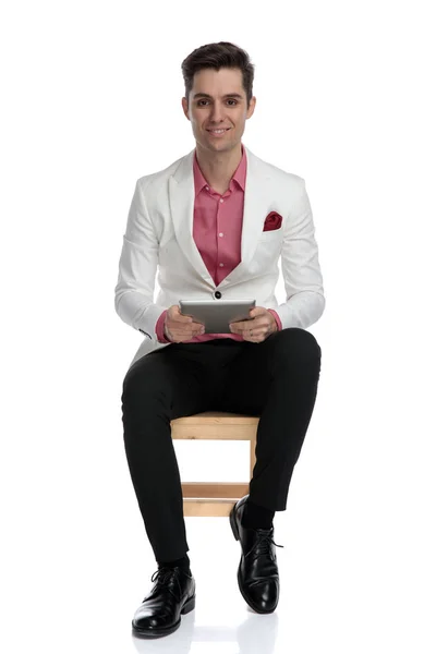 Sorrindo homem elegante segurando um tablet enquanto sentado na cadeira — Fotografia de Stock