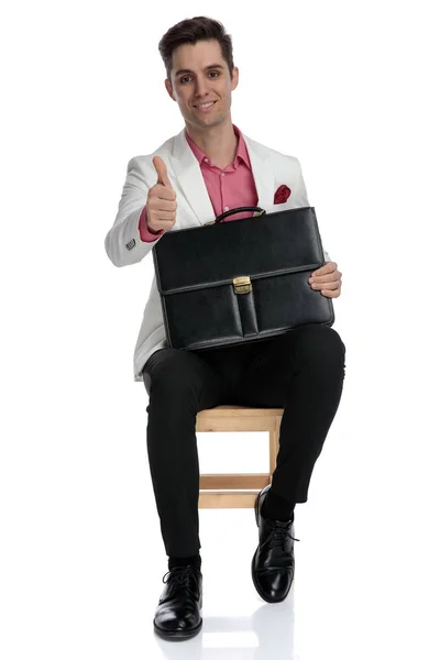 Oturma ve bavul tutan genç işadamı ok işareti yapar — Stok fotoğraf