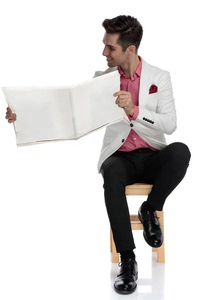 Sorrindo homem elegante mostrando jornal para o lado enquanto sentado — Fotografia de Stock