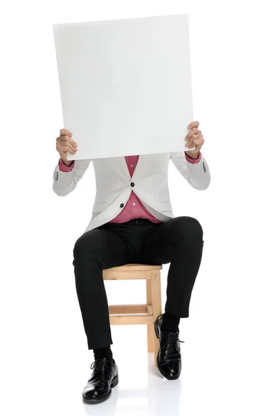 Homem sentado elegante se esconde atrás de uma placa em branco — Fotografia de Stock