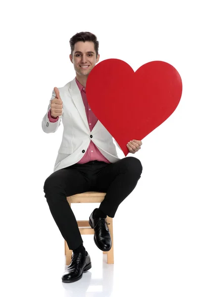 Hombre elegante joven positivo hace signo aceptable mientras sostiene el corazón — Foto de Stock