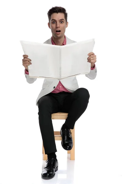 Shoked elegant man reading newspaper while sitting on chair — Stock Photo, Image