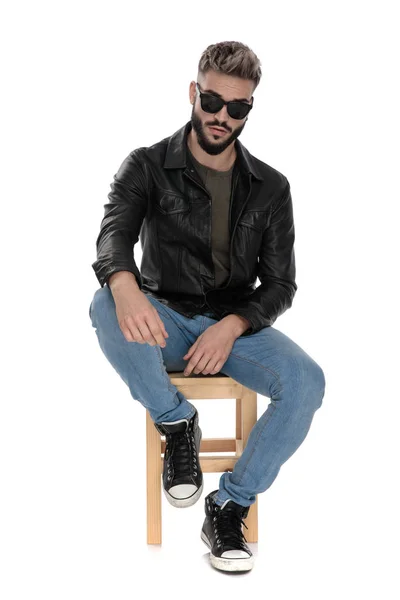 Man in black jacket and blue jeans with arm on knee — Stock Photo, Image