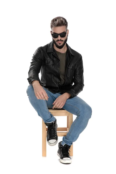 Man in black jacket and blue jeans with arm on knee — Stock Photo, Image