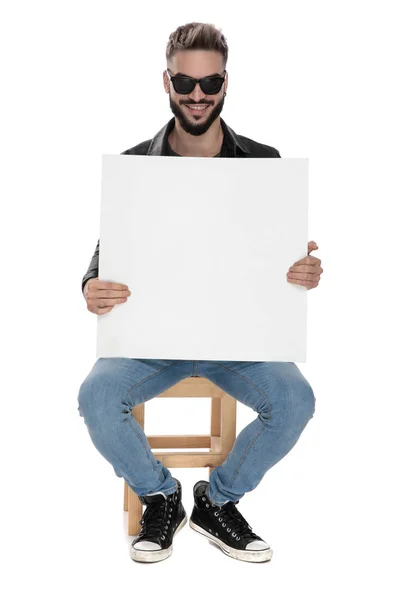 Mann sitzt auf Stuhl und hält eine leere Plakatwand — Stockfoto