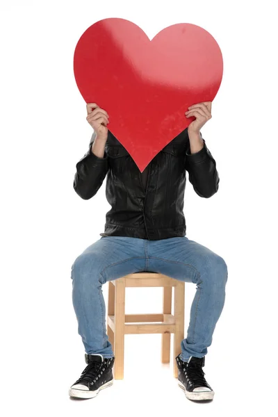 Uomo che tiene il cuore rosso a portata di mano mentre si copre il viso — Foto Stock