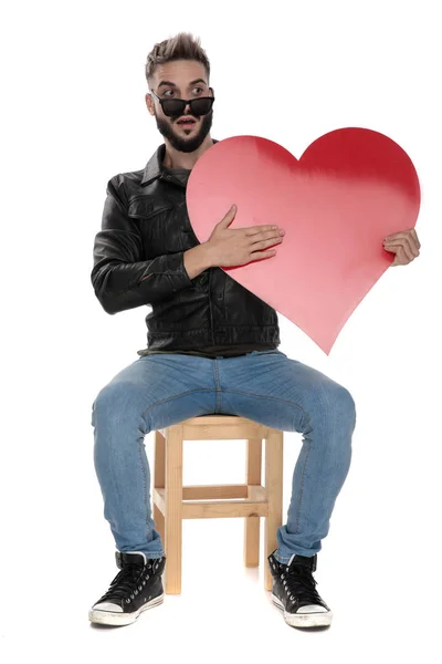 Homem segurando um coração vermelho na mão enquanto olha espantado — Fotografia de Stock