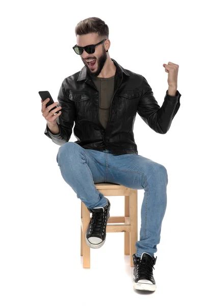 Man sitter på stol medan du tittar på telefonen firar — Stockfoto