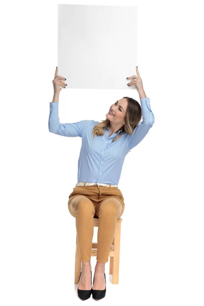 Seated businesswoman casually-dressed holds board and looks up — Stock Photo, Image