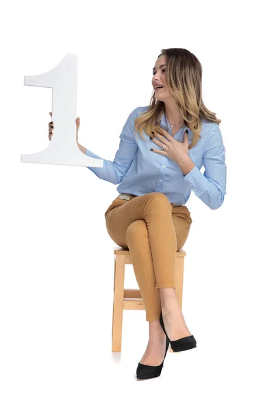 Счастливая деловая женщина сидит и смотрит на знак номер один — стоковое фото