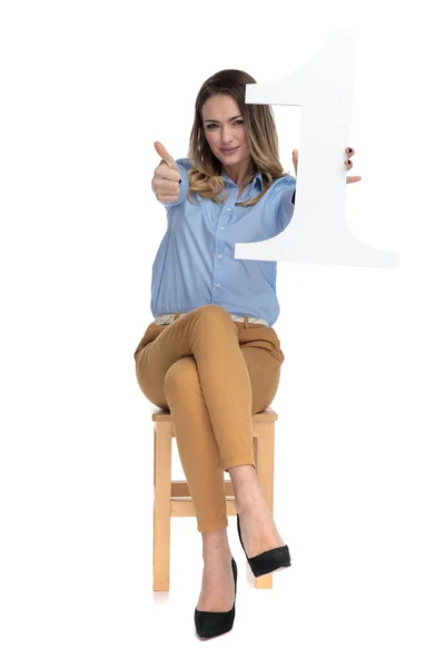 Непринужденно одетая женщина держит знак номер один и показывает большие пальцы вверх — стоковое фото