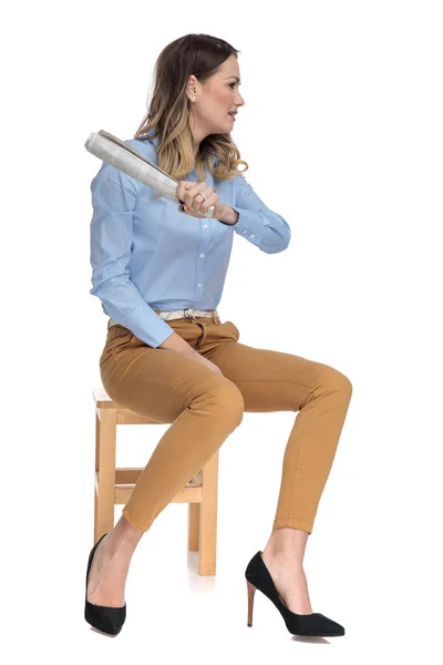 Smart casual woman holding a rolled newspaper sits on wooden cha — Stock Photo, Image