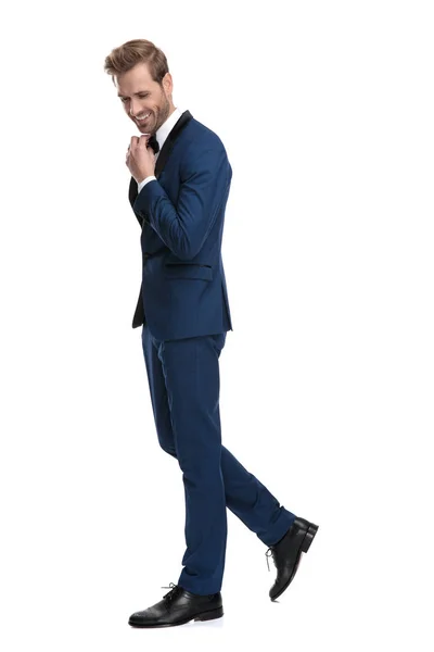 Attractive man in blue suit walking and adjusting his bowtie — Stock Photo, Image