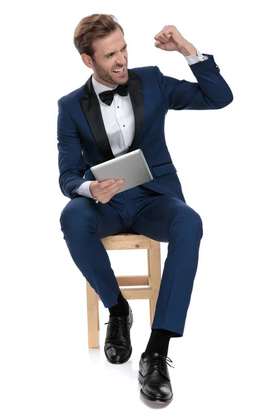 Happy man celebrating victory while sitting with notepad in hand — Stock Photo, Image