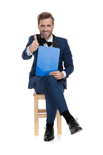 Sedící elegantní muž ukazuje ok gesto podržíte schránky — Stock fotografie
