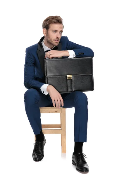 Siedzą stylowy mężczyzna jest w stanie spoczynku rękę na czarny walizka — Zdjęcie stockowe