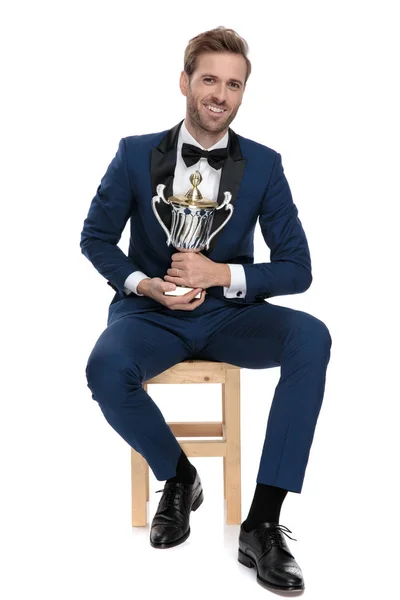 Sittande affärsman innehar trophy cup med båda händerna — Stockfoto