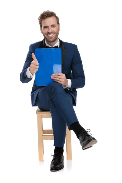 Sitzender eleganter Mann zeigt ok Geste, während er ein Klemmbrett hält — Stockfoto