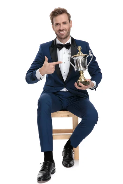 Seated happy man is pointing his finger to trophy cup — Stock Photo, Image