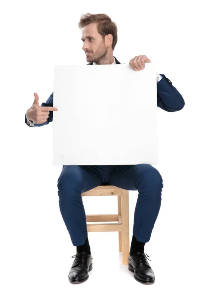 Сидить гордий хлопець вказує пальцем на порожній рекламний щит — стокове фото