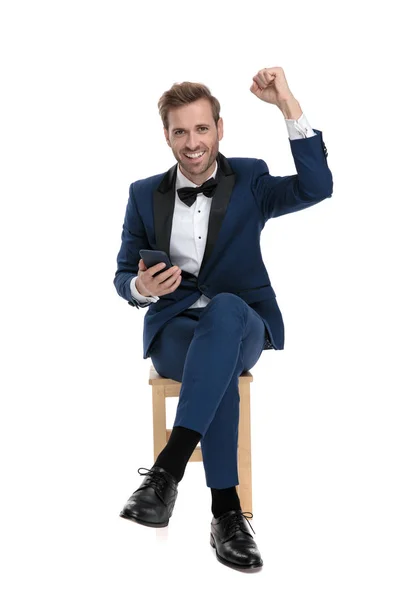 Seated gentleman celebrating victory while holding a mobile phon — Stock Photo, Image