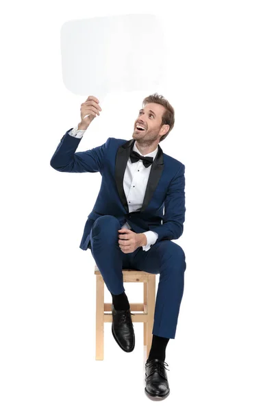 Siedzący szczęśliwy człowiek trzyma czat bubble w powietrzu — Zdjęcie stockowe
