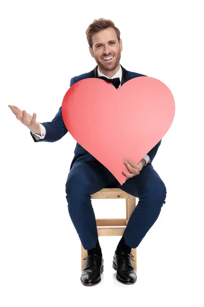Sitzender gutaussehender Mann mit rotem Herz in den Händen — Stockfoto